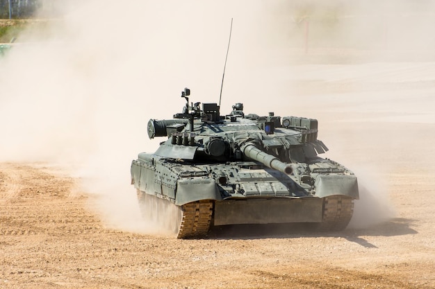 Foto potente tanque militar cabalga a gran velocidad a lo largo del campo polvoriento.