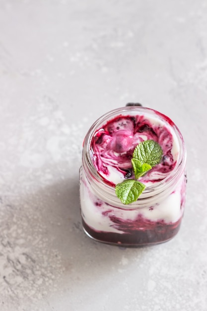 Potes de iogurte natural com molho de bagas e hortelã na mesa cinza clara. Alimentação saudável. Copie o espaço. Conceito de comida de verão.
