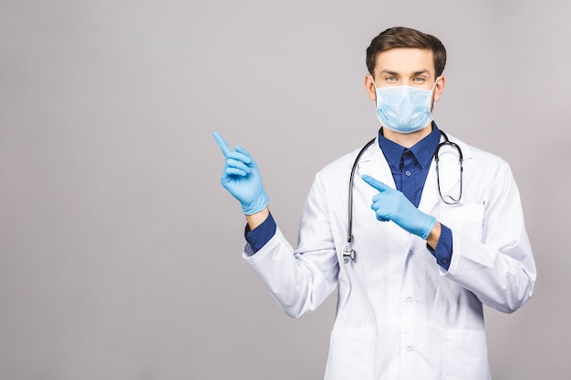 Potrait de guapo médico con máscara protectora quirúrgica y guantes azules Señalando con el dedo.