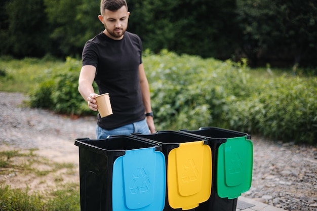 Potrait del hombre arrojando una taza de cartón vacía de capuchino en contenedores de reciclaje de árboles de papelera de reciclaje