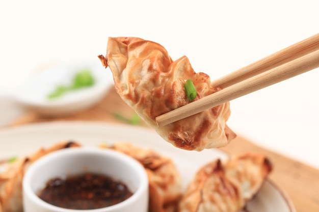 Potstickers asiáticos Gyoza con salsas servidos en un plato estilo japonés de cerámica marrón con palillos y cebolleta sobre fondo de madera blanca. Cocción de Airfryer sin aceite.