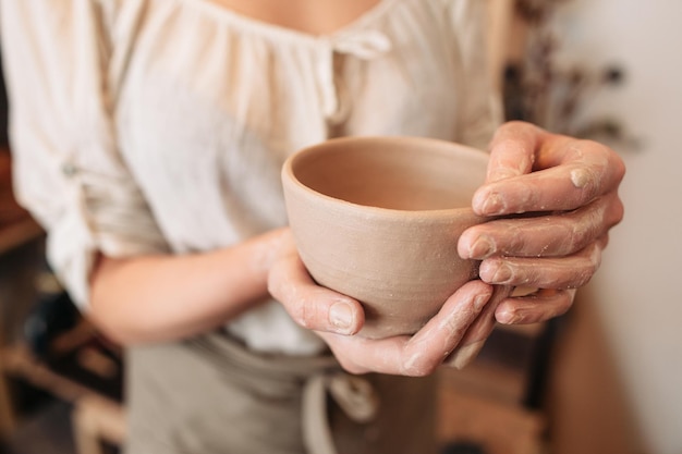 Potter mujer manteniendo cuenco de arcilla en palmas sucias