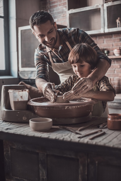 Pottering con padre. Joven alegre y niño haciendo vasija de cerámica en la clase de alfarería