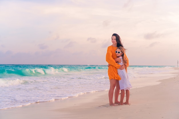 Pouco linda garota e jovem mãe na praia tropical