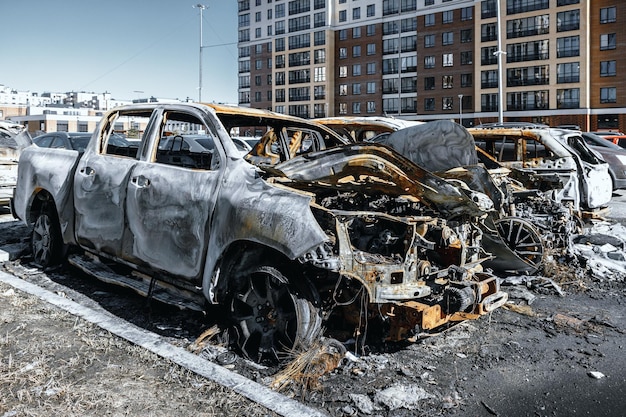Poucos carros queimados no estacionamento perto de edifícios Veículos não recuperáveis destruídos pelo fogo