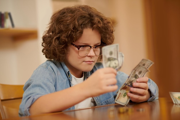 Poupança. Um menino de óculos e camisa jeans contando suas economias e parecendo sério