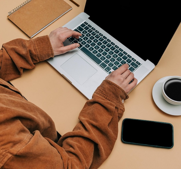 POV-Ansicht auf Frau übergibt Laptop-Computer neben Tasse Kaffee und Handy auf braunem Hintergrund