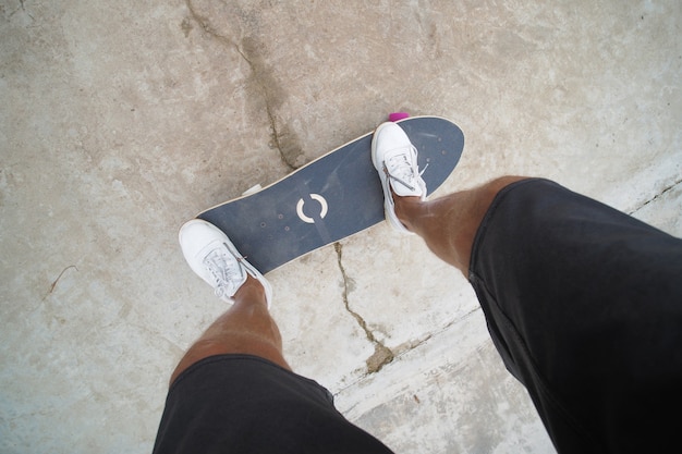 POV-Ansicht. Männliche Füße tragen weiße Turnschuhe auf Skateboard im Park.