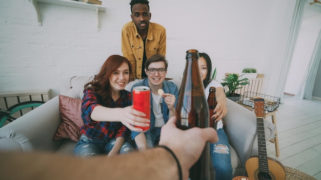 Foto pov-aufnahme einer männlichen hand, die mit freunden eine bierflasche anstößt, während sie zu hause drinnen eine party feiert