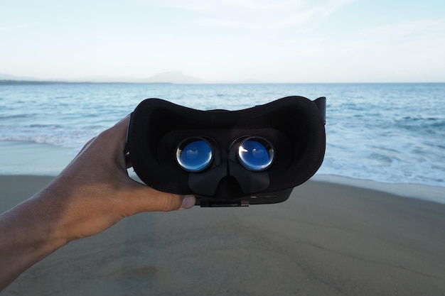 POV-Aufnahme Virtual-Reality-Headset in den Händen am tropischen Strand neben dem Meer