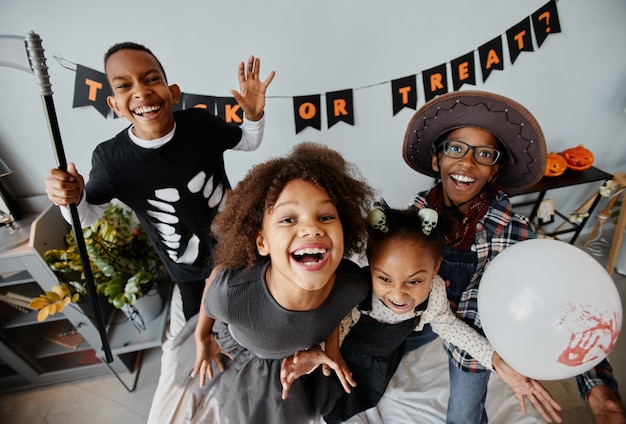 Pov-Aufnahme von aufgeregten afroamerikanischen Kindern, die zu Hause Halloween-Kostüme tragen und in die Kamera schauen