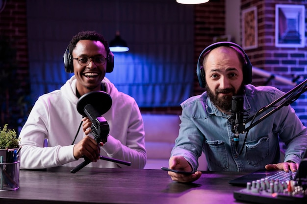 Pov de influenciadores masculinos gravando chat de podcast na câmera, usando equipamento de streaming em estúdio com luzes de neon. criadores de conteúdo se divertindo filmando episódios online para mídias sociais.