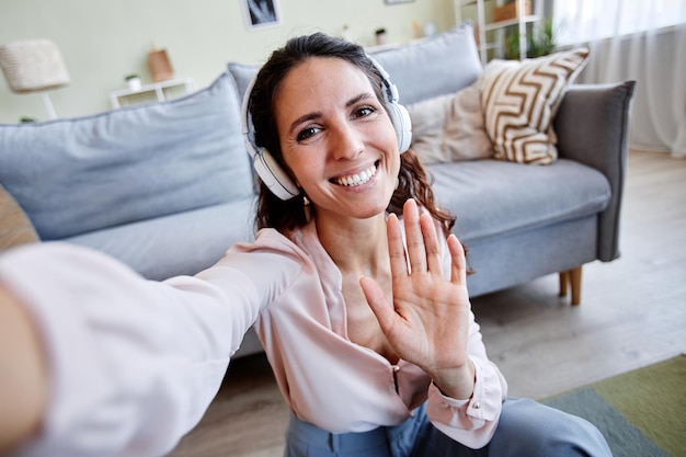 Foto pov de uma mulher sorridente acenando para a câmera gravando vídeo ou transmissão ao vivo em casa