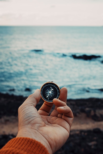 Foto pov de hombre con la mano sosteniendo la brújula de viaje de navegación para encontrar la dirección y el siguiente lugar de destino concepto de personas que viajan y exploran la playa y el océano con luz del cielo en el fondo