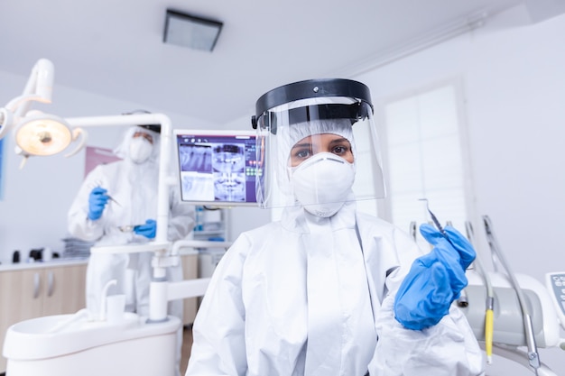 Pov paciente de dentista segurando a ferramenta para tratamento de dentes em consultório odontológico. Stomatolog usando equipamento de segurança contra coronavírus durante a verificação de cuidados de saúde do paciente.