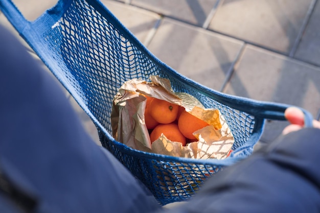 POV viele Orangen in Papiertüten in blauer, handgefertigter Mesh-Einkaufstasche. Nahaufnahme von oben mit Blick auf Früchte in einer Tasche