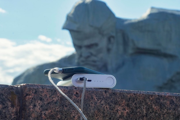 Power bank carrega um smartphone em frente a um monumento na fortaleza de brest