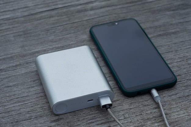 Power bank carrega um smartphone em um banco de madeira no parque.