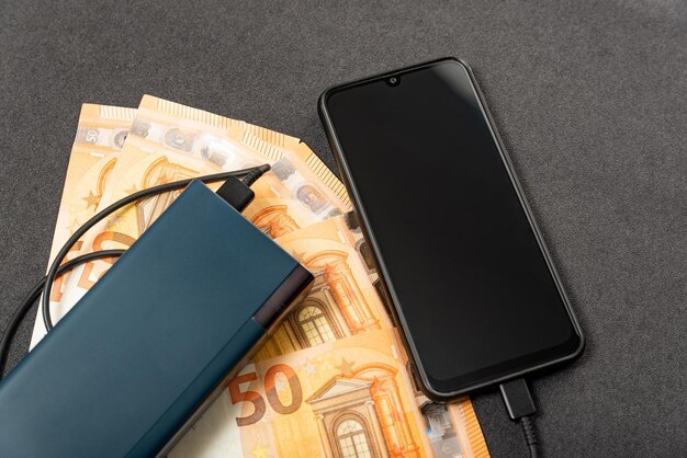 Power Bank Smartphone und Papierrechnungen Bargeld Euro auf grauem Hintergrund Gerätekauf Energiesparendes Gerät und Telefon