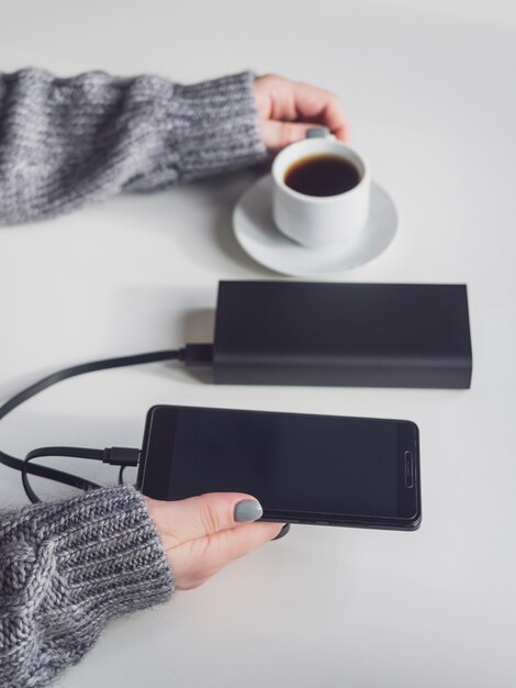 Power Bank und Telefon sind schwarz. Die Power Bank lädt das Telefon auf dem Tisch auf.