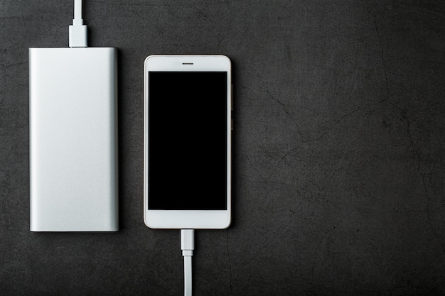 Un Powerbank blanco carga un teléfono inteligente. Batería externa universal para gadgets Espacio libre.