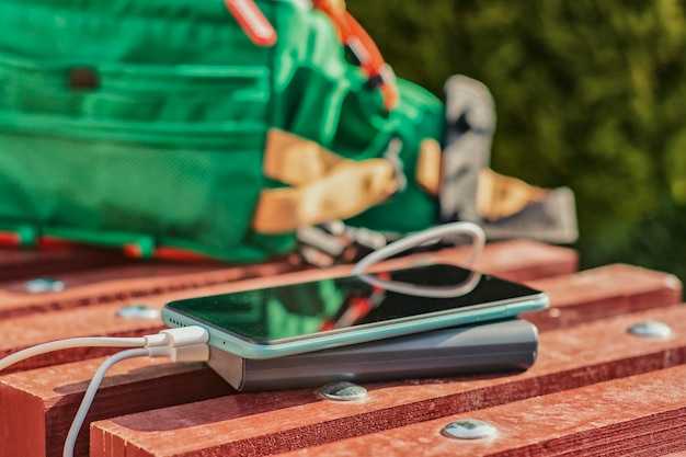 Foto powerbank lädt ein smartphone auf einer bank mit einer grünen tasche auf. tragbares ladegerät für gadgets
