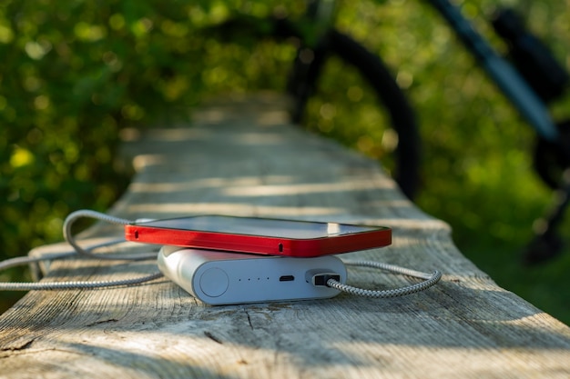 Powerbank lädt ein Smartphone im Wald vor dem Hintergrund eines Fahrrads auf.