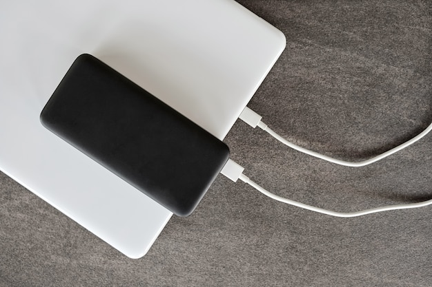 Foto powerbank lädt einen laptop über ein usb-typ-c-kabel auf grauem steinhintergrund auf