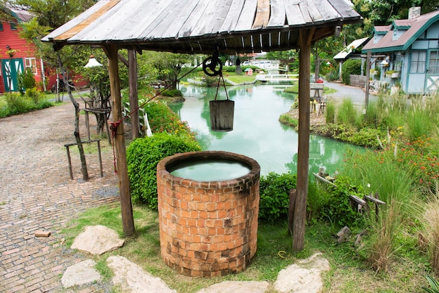 Pozo de agua artesanal de ladrillo de piedra antiguo retro clásico y carrete de cubo de madera con cuerda para uso de los tailandeses en el parque de jardín al aire libre en el campo rural en Nonthaburi Tailandia