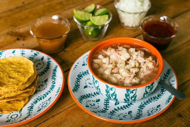 Pozole servido em um prato fundo com tostadas salsa e legumes em uma mesa de madeira