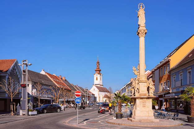 Praça principal com a estátua da peste e a Igreja na pequena cidade de Leibnitz, na Estíria, na Áustria. Vista de rua na cidade austríaca. Arquitetura do edifício.