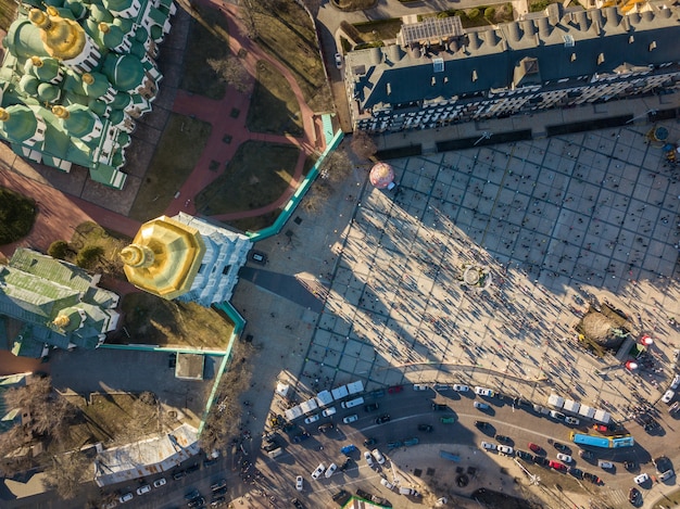 Praça Sophia e parte da igreja com muita gente e carros estacionados em dia de sol