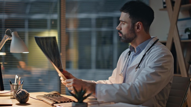 Practicante de la clínica trabajando de noche de cerca hombre serio médico examinando rayos X