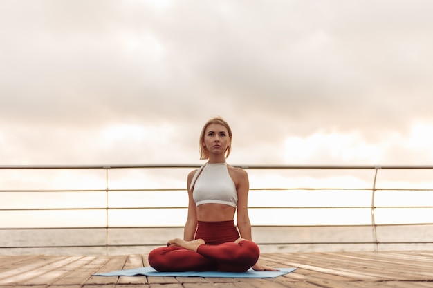 Practicar yoga en la mañana al aire libre yogui joven en ropa deportiva está sentado en posición de loto