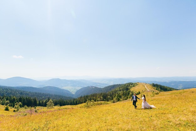 Prado con hierba verde en la cima de la montaña y recién casados que