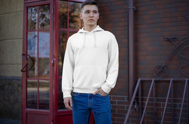 Präsentation eines weißen Hoodies auf einem jungen Mann auf der Straße, Vorderansicht. Mockup-Modekleidung für die Werbung im Laden. Muster für Freizeitkleidung für Ihr Design.