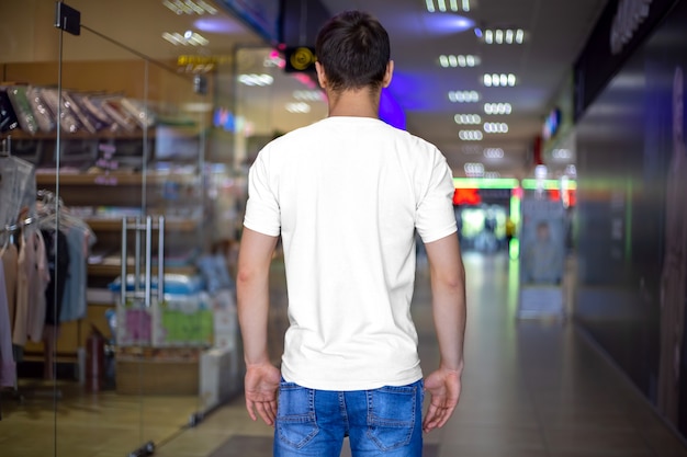 Präsentation eines weißen Mockup-T-Shirts an einem Mann, Rückansicht. Design-Vorlagenkleidung auf dem Hintergrund des Ladens, lässiger Stil.