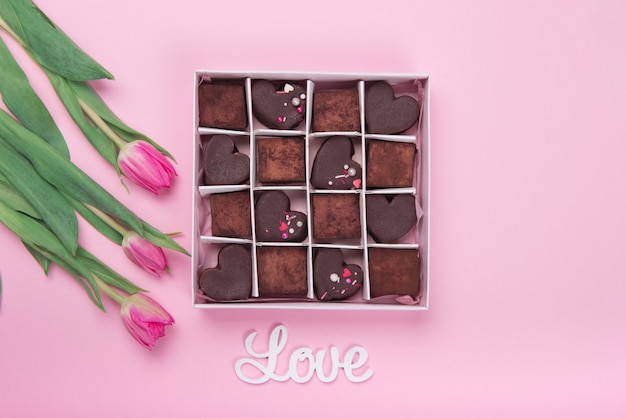 Präsentieren Sie Box mit Schokoladenbonbonsherzen und Tulpen auf rosa Hintergrund. Wüste zum Valentinstag