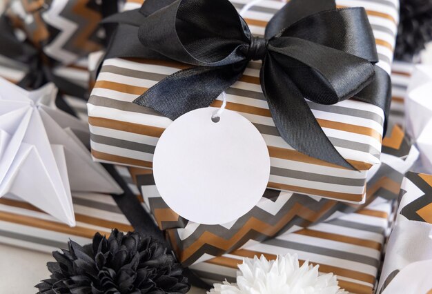 Präsentieren Sie mit leerem rundem Geschenkanhänger und schwarzer Schleife aus nächster Nähe Geschenkboxen, die in gestreiftes und Chevron-geometrisches Papier in der Nähe von Schwarz-Weiß-Dekor verpackt sind Weihnachten Neujahr Geburtstag Jubiläum Etikettenmodell