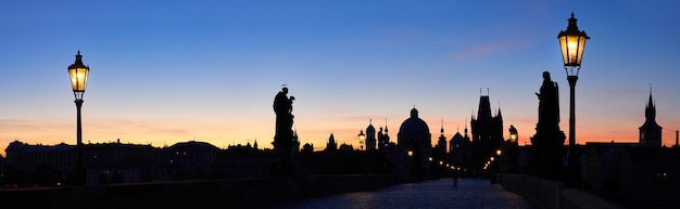 Prag, Karlsbrücke nachts mit rosa, lila Wolken des Sonnenaufgangs. Silhouetten des alten Brückenturms, der Kirchen und der Türme des alten Prags gegen den hellen Himmel. Panorama-Bannerbild.