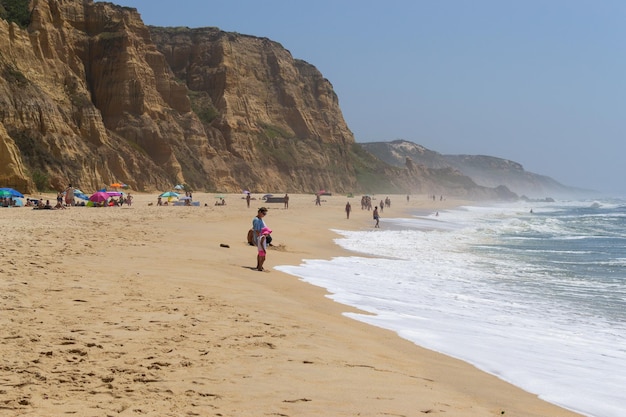 Praia à beira-mar com pessoas a descansar local de férias Montanhas mar e ondas Viajar para a Europa Portugal