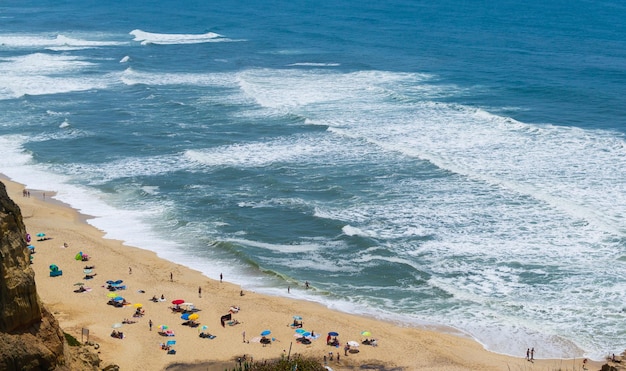 Praia à beira-mar com pessoas descansando local de férias Montanhas mar e ondas Viajar para a Europa Portugal