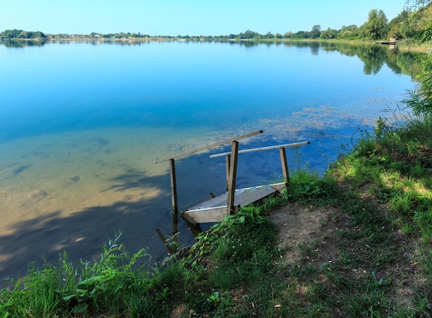 Praia calma do lago de verão com declives de madeira para a água