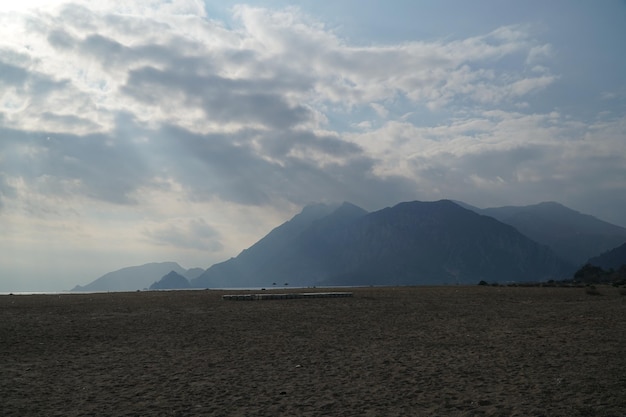 Praia com montanhas ao fundo e nuvens em Cirali