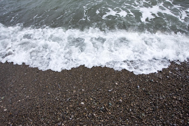 Praia com seixo rolado e mar com espuma