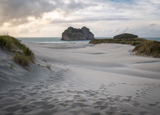 Praia com tiro de areia branca durante o pôr do sol na praia de wharariki, nova zelândia