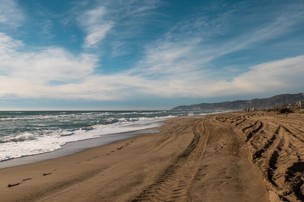 Foto praia de areia deserta com ondas espumosas e rastros de pneus sob um vasto céu azul