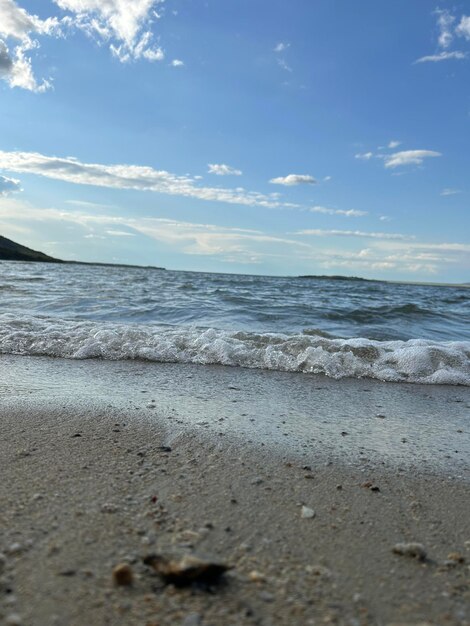 Praia de areia e mar azul de perto ondas suaves lamberam a praia de areia belas ondas do mar com espuma de