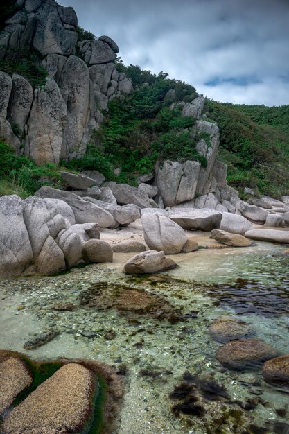 Praia de areia marinha com grandes pedras na costa e água clara