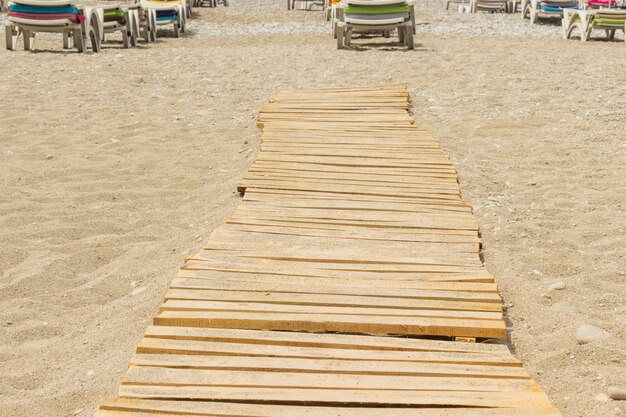 Praia de areia, tábuas de madeira e espreguiçadeiras à distância